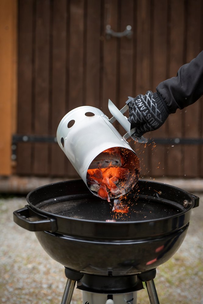 Grillhandschuh beim Anzünden  glühende Holzkohle wird aus Anzündkamin in Kugelgrill geschüttet