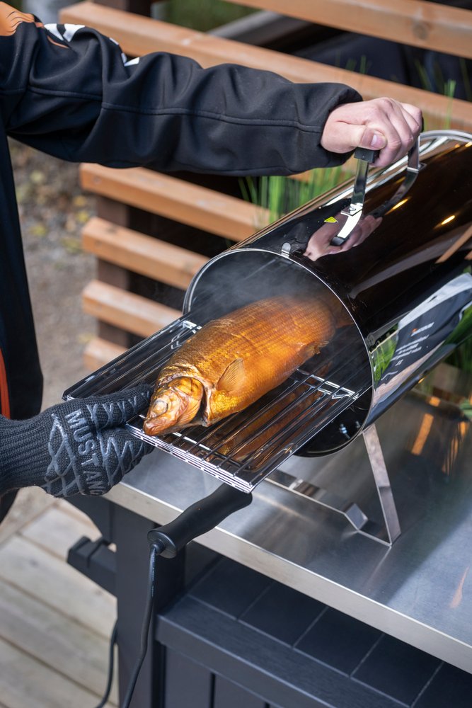 Mustang Grillhandschuh beim Räuchern - geräucherte Forelle wird aus Räucherofen entnommen, Lifestyle-Aufnahme