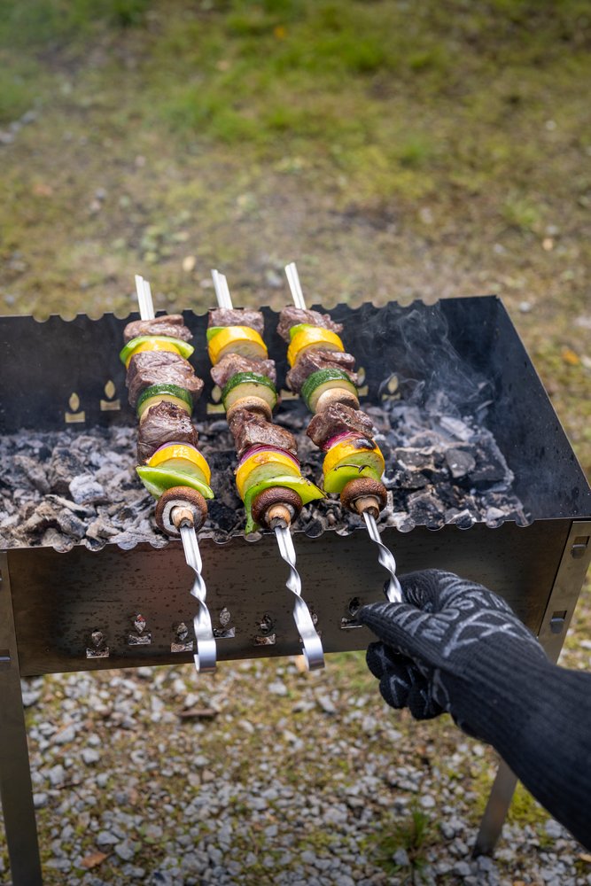 Mustang Grillhandschuh beim Schaschlik-Grillen - Spieße auf Mangal-Grill werden mit schwarzem Handschuh gewendet