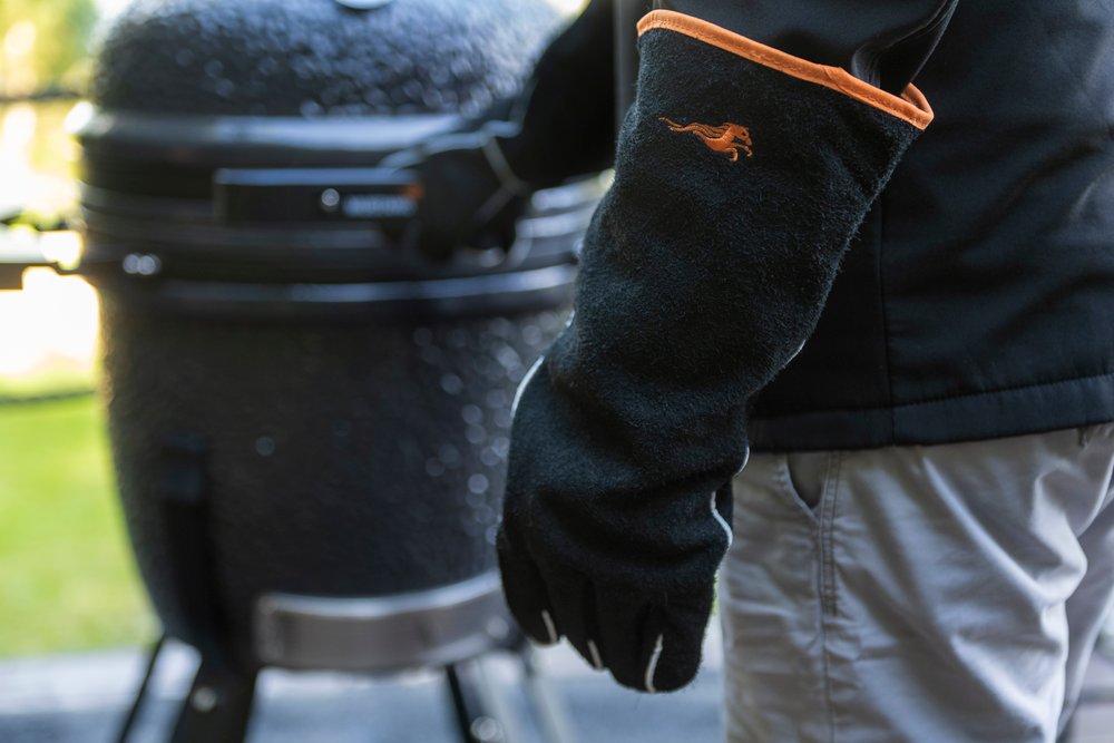 Mustang Leder-Grillhandschuh im Einsatz - Person trägt schwarzen Lederhandschuh neben Kamado-Grill, Lifestyle-Aufnahme