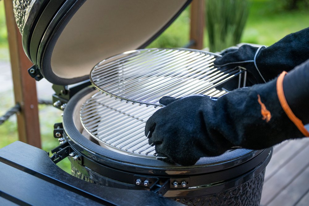 Mustang Leder-Grillhandschuhe beim Kamado-Grillen - beide Hände heben Grillrost aus geöffnetem Keramikgrill, EN407 Hitzeschutz