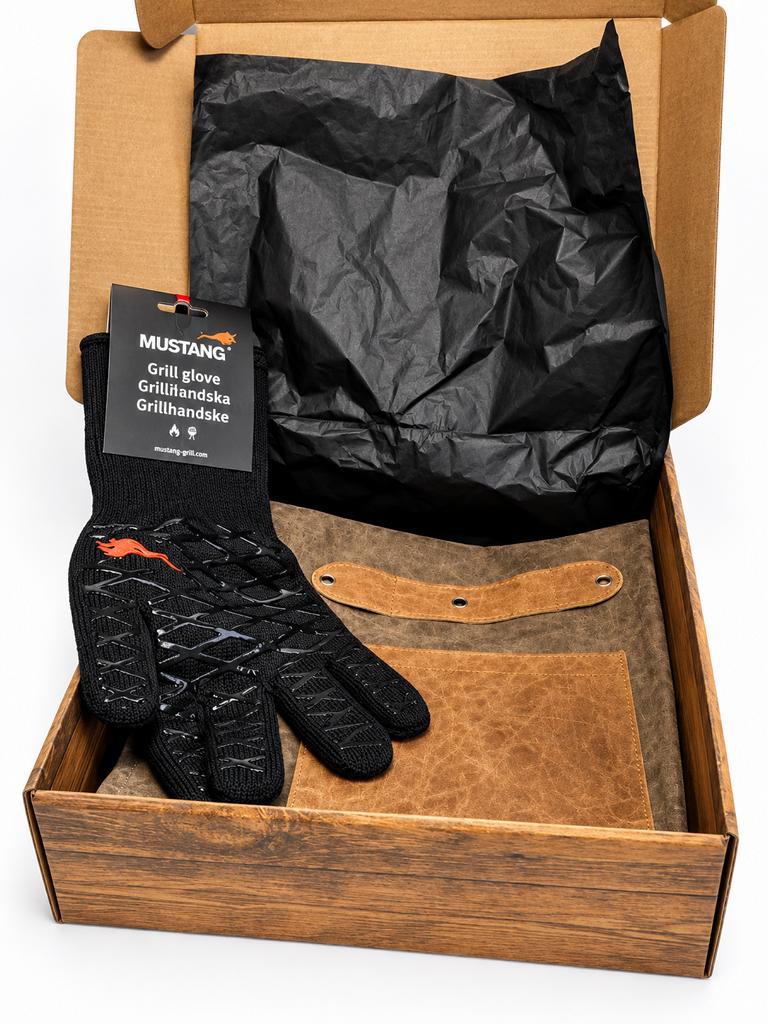 Geöffnete Grill-Geschenkbox mit einem schwarzen Mustang BBQ-Grillhandschuh und brauner Grillschürze aus Lederimitat